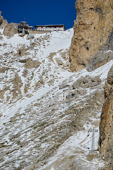 The Toni Demetz Hütte between the rocky Langkofeleck and the Fünffingerspitze with some snow and a blue sky. 