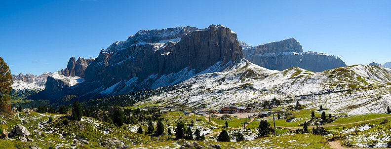 Steep mountains of the Sella Group rise up against a blue sky from the green meadows alongside the Sella Pass